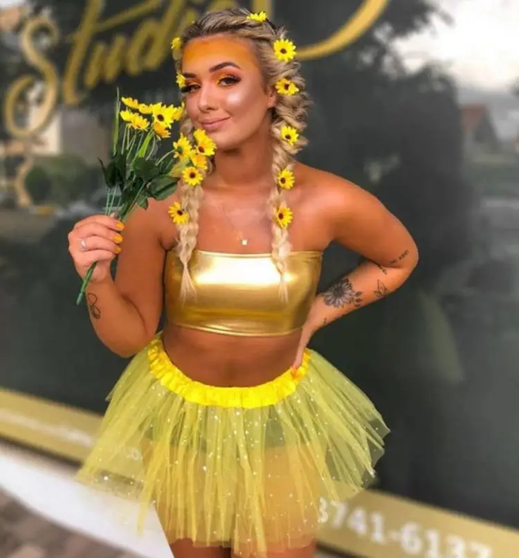 Mulher de pele clara suando top dourado, saia amarela de tule e girassóis no cabelo
