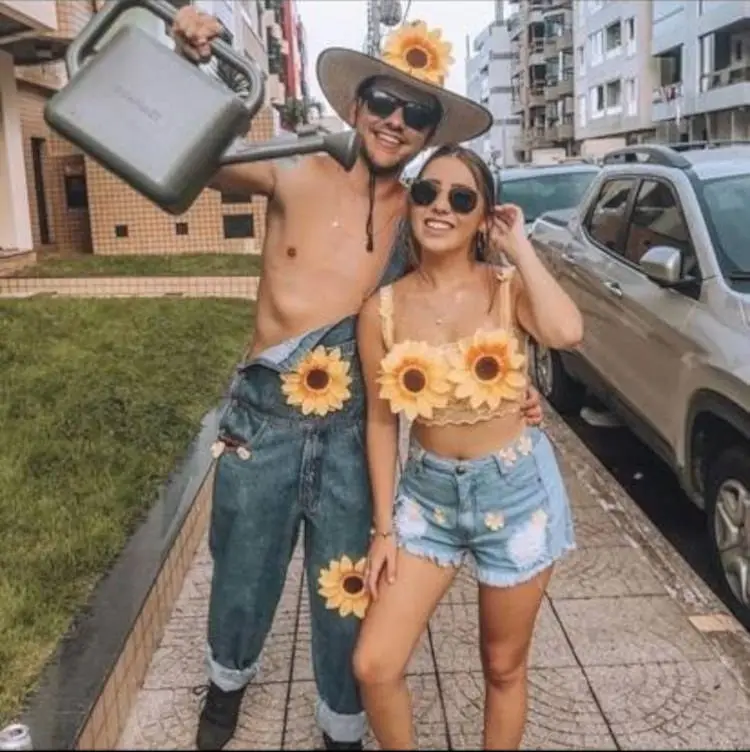 Homem de pele clara de jardineira, regador e chapéu e mulher de pele clara de cropped de girassol e shorts jeans