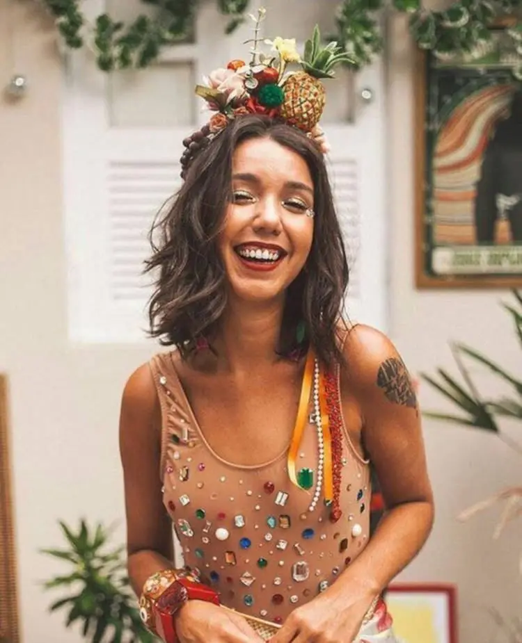 Mulher de pele clara com tiara de frutas e body bege com pedrarias