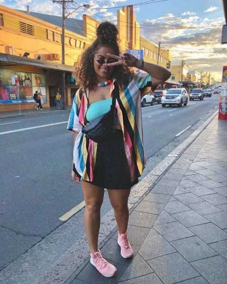Mulher de pele negra com top azul, saia preta e kimono colorido 