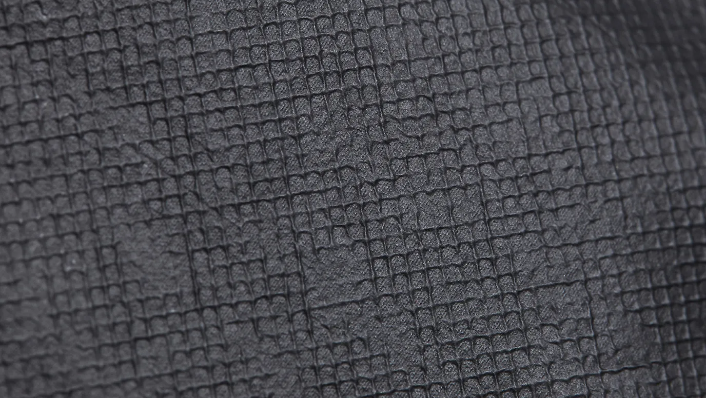 Close-up da superfície de uma peça de grafeno, mostrando uma textura de grade em relevo. O material é cinza-escuro e tem uma aparência granulada.