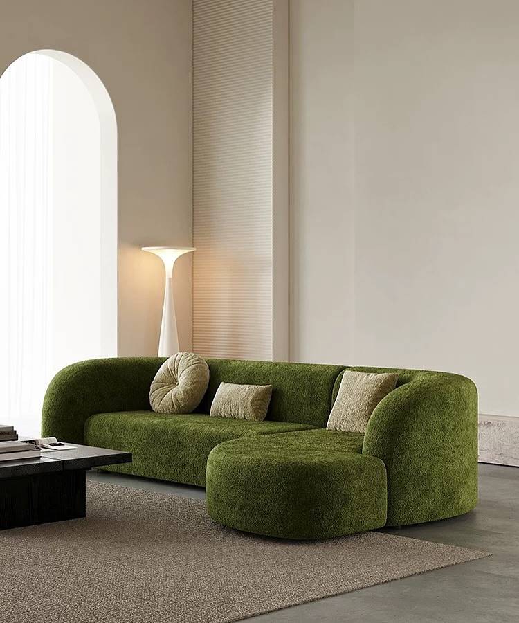 Uma sala minimalista e moderna com um sofá verde musgo curvado e um pufe combinando. As almofadas para sala em tons neutros complementam o estofamento texturizado. Ao fundo, um arco elegante e uma luminária de piso escultural. O ambiente exala design contemporâneo e sofisticação.







