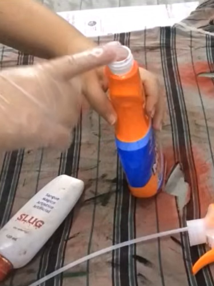 Mulher de pele clara com luvas segurando borrifador ao lado de embalagem branca de sangue falso 