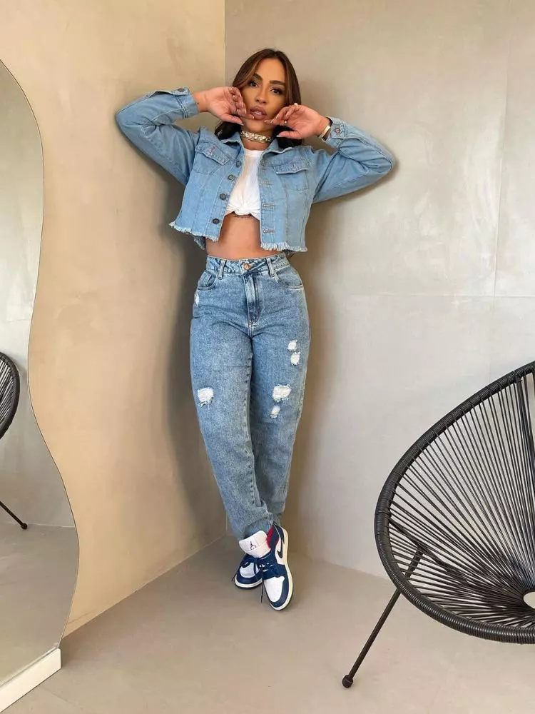 Mulher de pele clara com top branco, jaqueta jeans e mom jeans