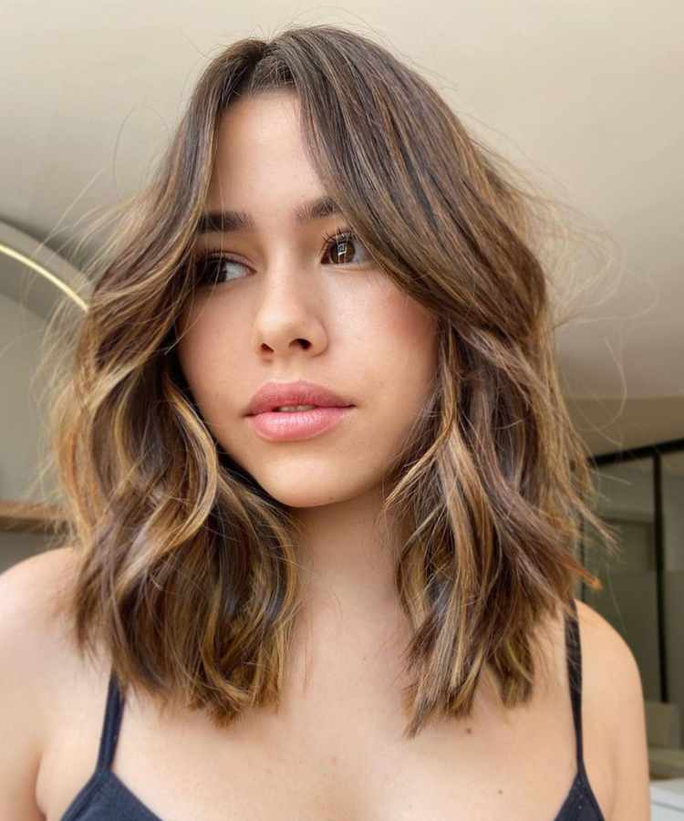 Corte de cabelo médio com franja curtain bangs.