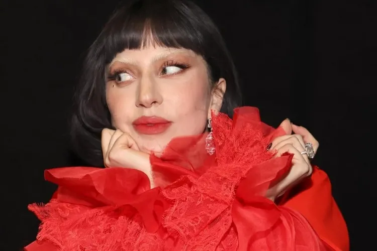 Foto da cantora Lady Gaga de cabelo preto chanel com franja, sobrancelhas descoloridas e blusa vermelha com babados