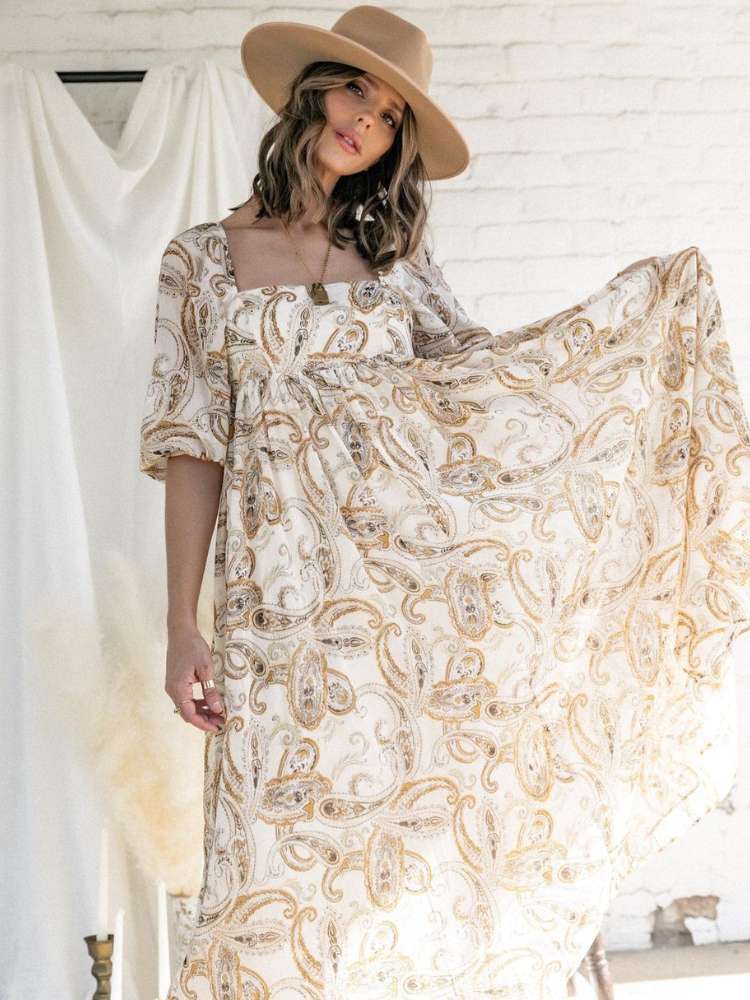 Mulher de pele clara usando chapéu aba reta e vestido decote quadrado e estampa boho 
