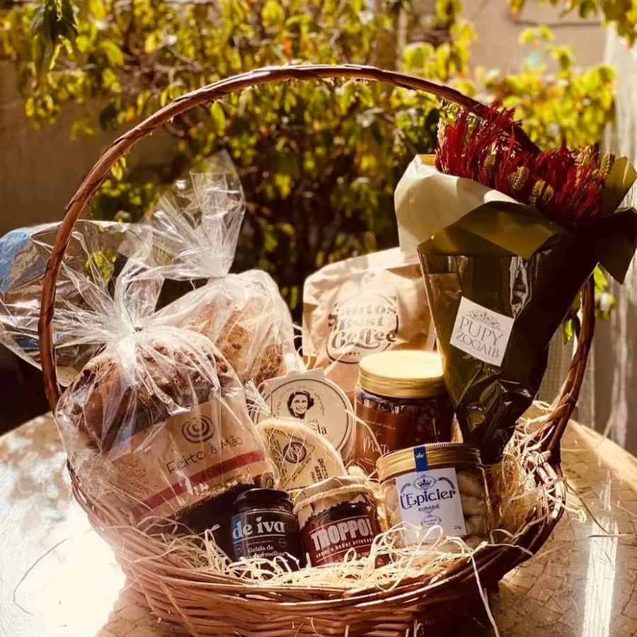 Foto de cestona feita à mão com brioche, pão italiano, café, geleia, biscoito e arranjo. 