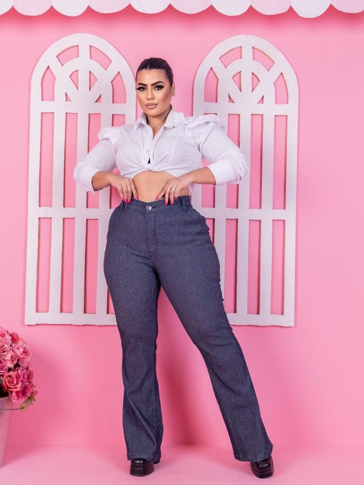 Mulher de pele clara usando camisa branca amarrada e calça flare com detalhes em risca de giz