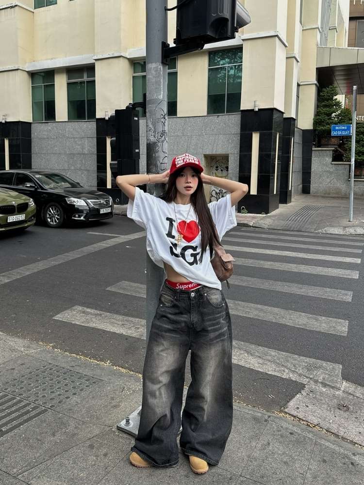 Mulher asiática usando blusão branco, jeans barrel escuro, boné, acessórios 