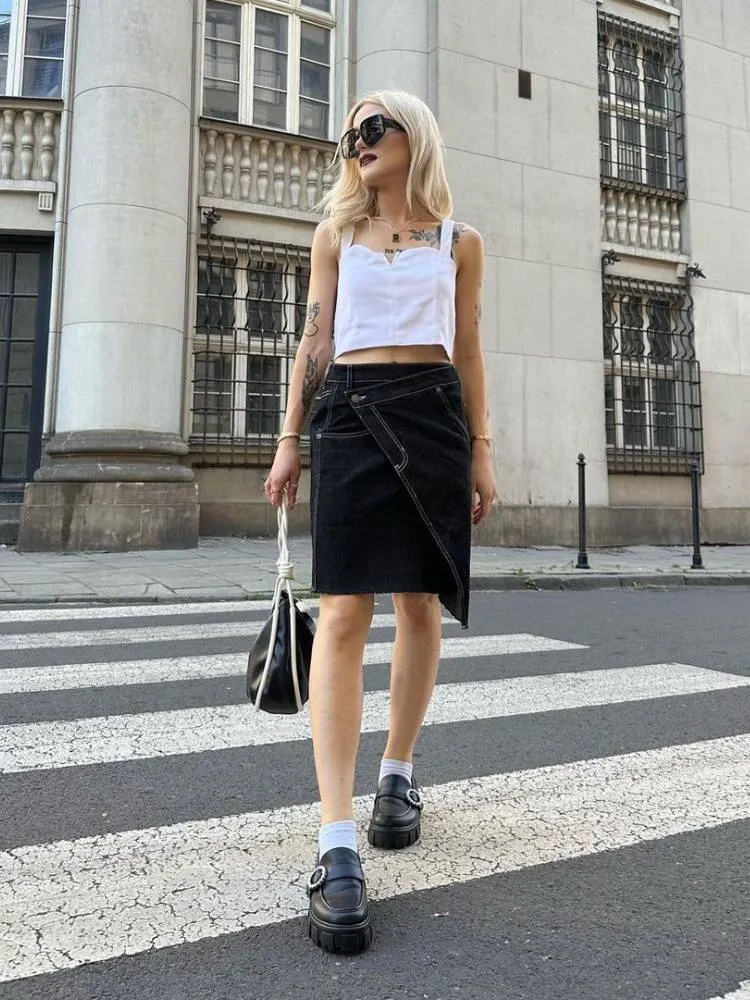 mulher usando cropped branco, saia jeans assimétrica, meia branca e mocassim com fivela lateral