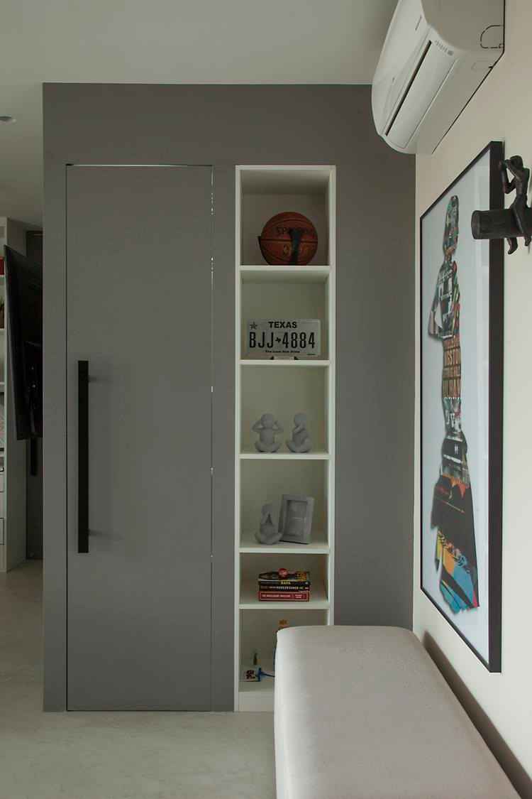 foto de porta branca com puxador preto, prateleira de nichos com itens como placa e bola de basquete, banco branco e quadro colorido ao lado