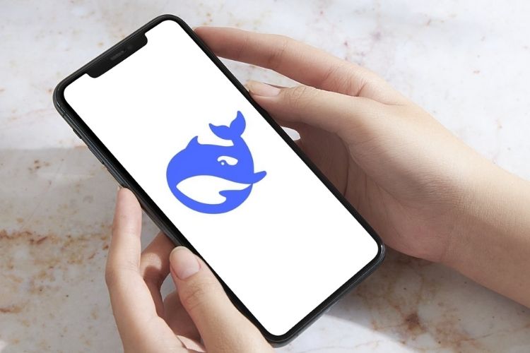 A imagem mostra mãos segurando um smartphone que exibe um logotipo azul de uma baleia em fundo branco. O fundo é uma superfície marmorizada clara, criando um contraste limpo e minimalista com o dispositivo e o logo.