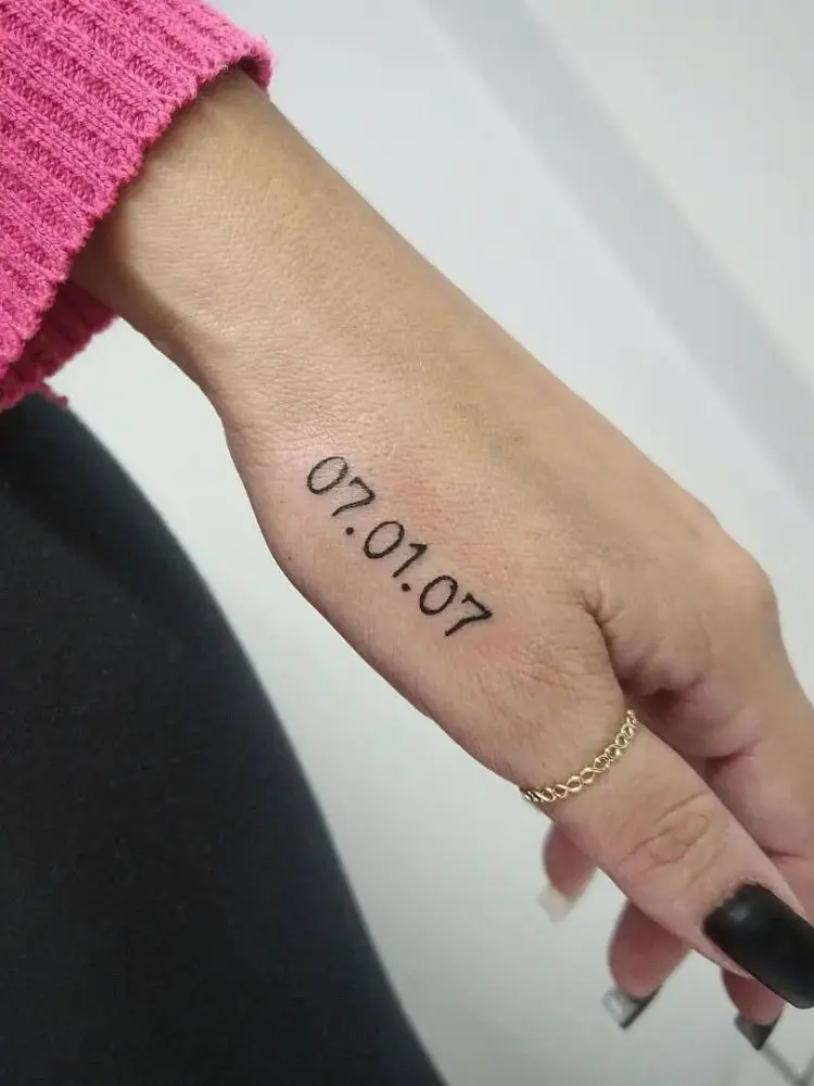 Mão de pele clara com tatuagem "07.01.07" no dedão