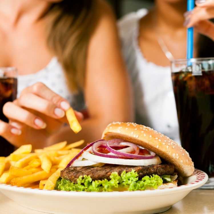 Duas meninas comendo um combo de hambúrguer com batata frita e refrigerante