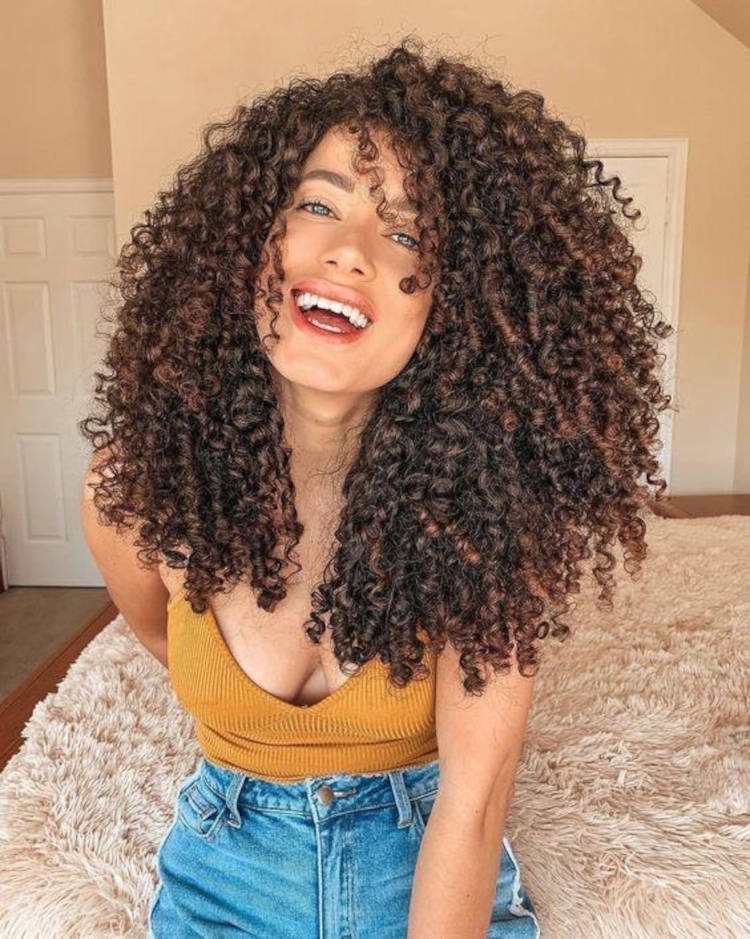 Mulher de pele morena com cabelo cacheado castanho volumoso solto 