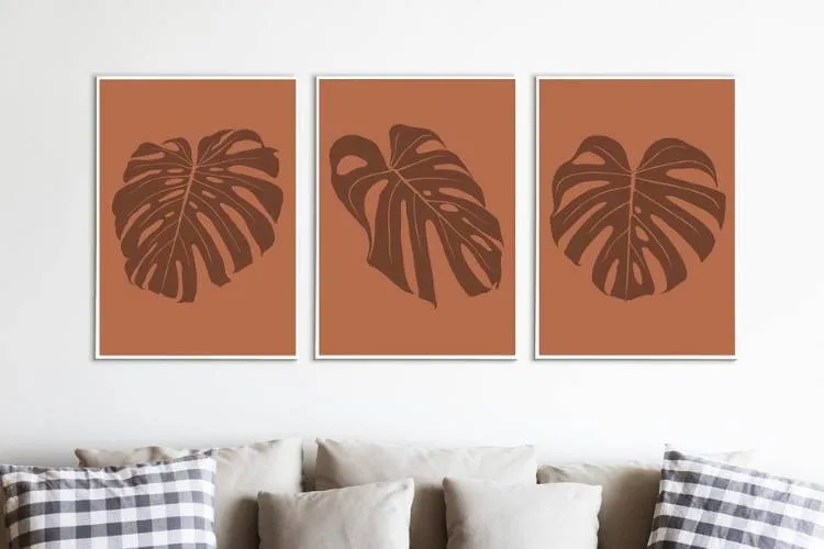 3 quadros em diferentes ângulos em tons terrosos sobre sofá cinza com almofadas cinzas e quadriculadas em preto e branco. 