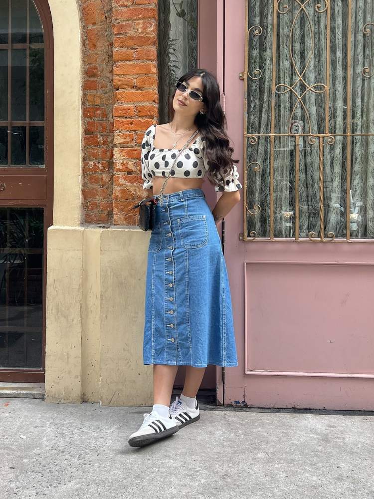 Victória de cropped branco de bolinhas pretas, saiai midi jeans, tênis e acessórios 