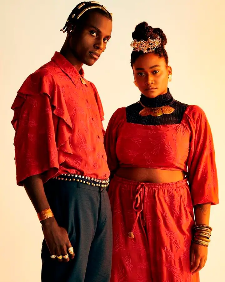 Casal de modelos. Ele usa uma blusa vermelha e calça escura. Ela usa blusa e calça vermelhas.