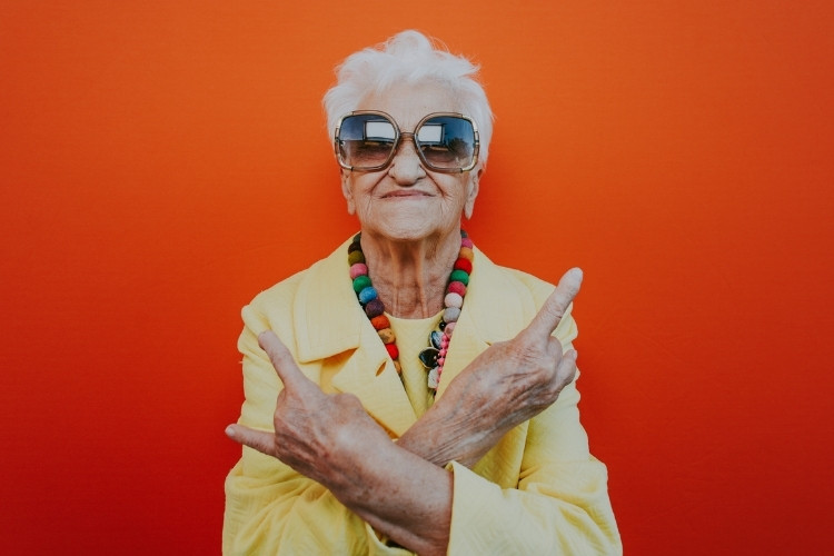 Foto de mulher idosa usando roupas coloridas e fazendo sinais de rock com as mãos