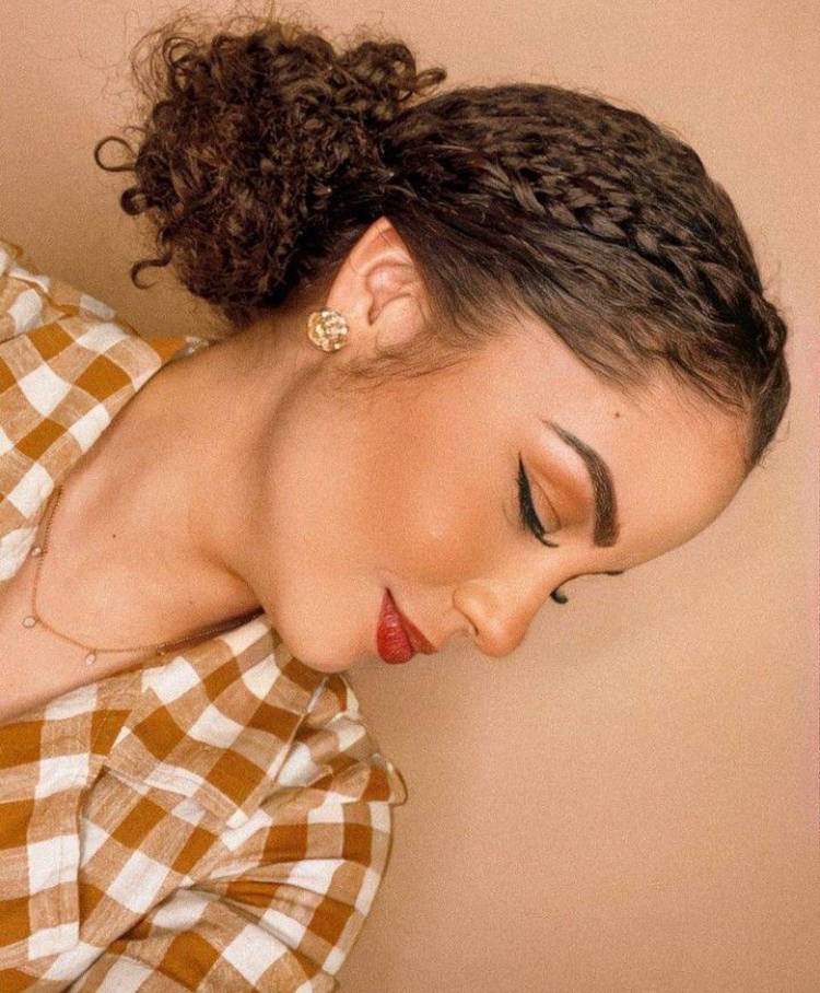 Mulher de pele clara com cabelo castanho cacheado em coque baixo com trança 