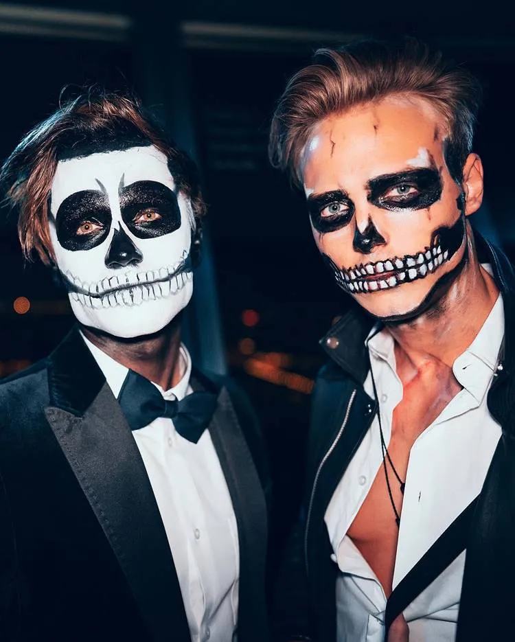 2 homens maquiados de caveira para o Halloween; ambos usando camisa branca e terno preto 