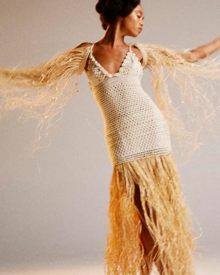 Modelo com um vestido de tricot bege com detalhes em palha.