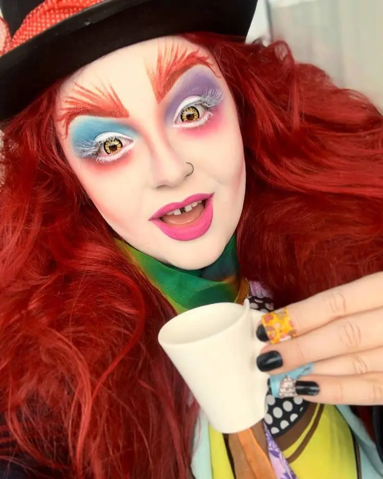 Pessoa com fantasia e maquiagem de Chapeleiro Maluco, com sombra azul e roxa, batom rosa e sobrancelha ruiva