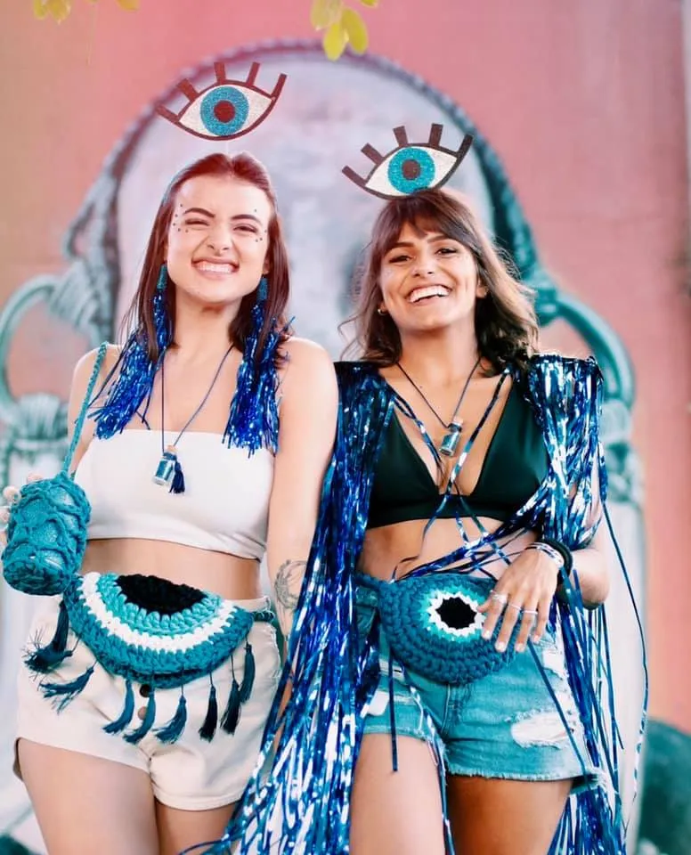 Duas mulheres de pele clara fantasiadas de olho grego