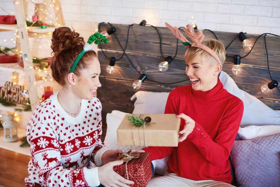 Foto de duas garotas de pele clara usando sueteres e trocando presentes no amigo ladrão de Natal.