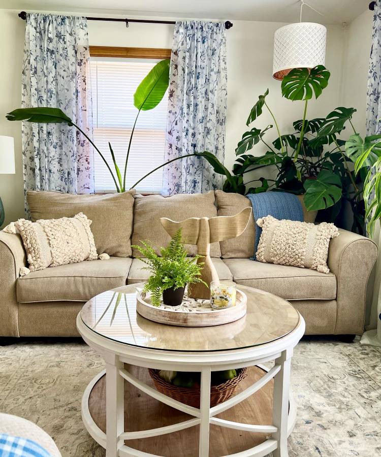 Sala de estar decorada com mesinha de centro, cortina, lustre e plantas
