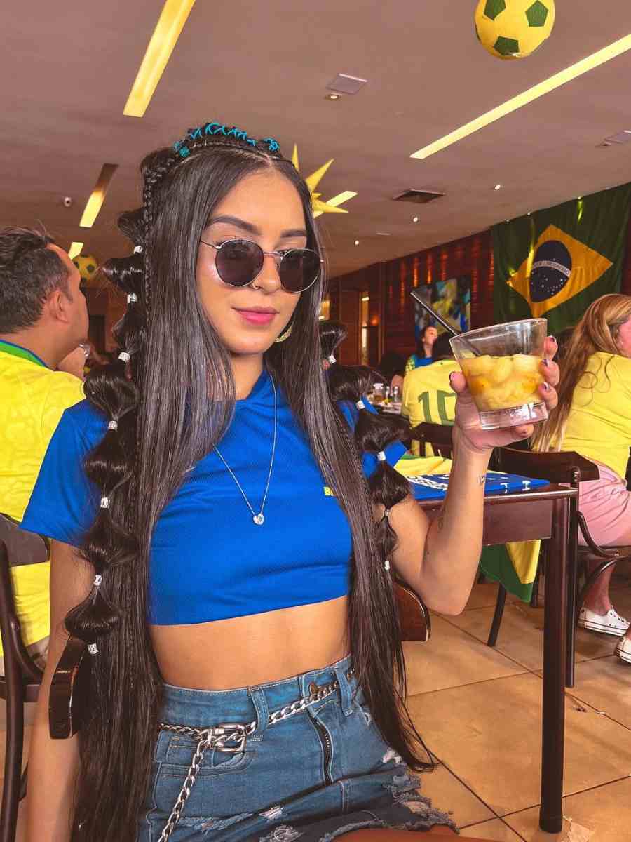 Foto de mulher com cropped azul do Brasil + saia jeans em barzinho.