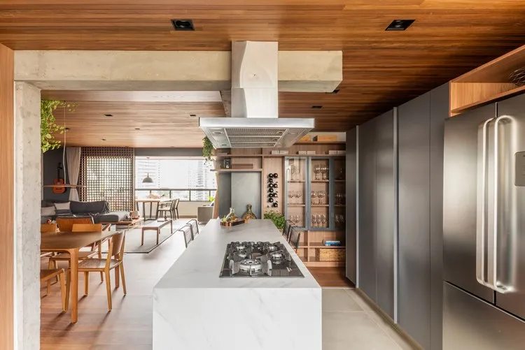 Cozinha de apê de 187 m² decorada pelo arquiteto Pietro Terlizzi, com ilha de mármore com cooktop e coifa em cima, eletrodomésticos em cor inox, cristaleira