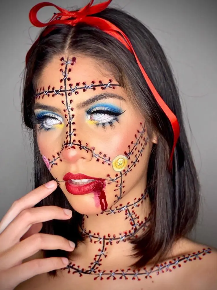 Mulher de pele clara com lente branca, rosto imitando costurado com sangue falso, desenho de botão, sombra azul e sangue falso na boca