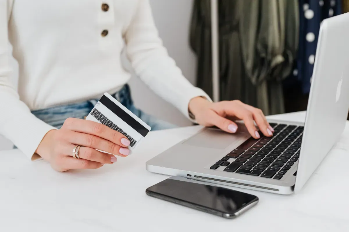 Pessoa segurando cartão bancário enquanto utiliza notebook para contratar serviço financeiro online com segurança.