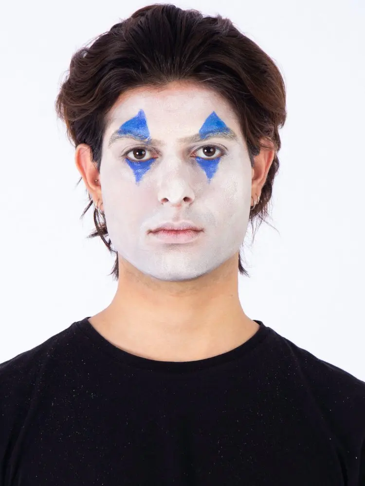 Homem de pele clara, cabelo médio castanho, usando blusa preta, pancake branco no rosto e clown azul nos olhos 