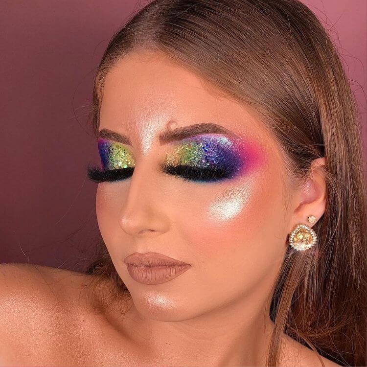 Mulher de pele clara com maquiagem glow, batom nude e olhos marcados com amarelo, verde, roxo e rosa
