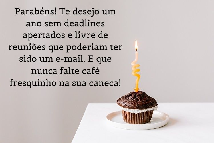 cartão virtual de feliz aniversário para colega de trabalho de fundo roxo, com mesa branca e cupcake com vela, além de frase "Parabéns! Te desejo um ano sem deadlines apertados e livre de reuniões que poderiam ter sido um e-mail. E que nunca falte café fresquinho na sua caneca!"