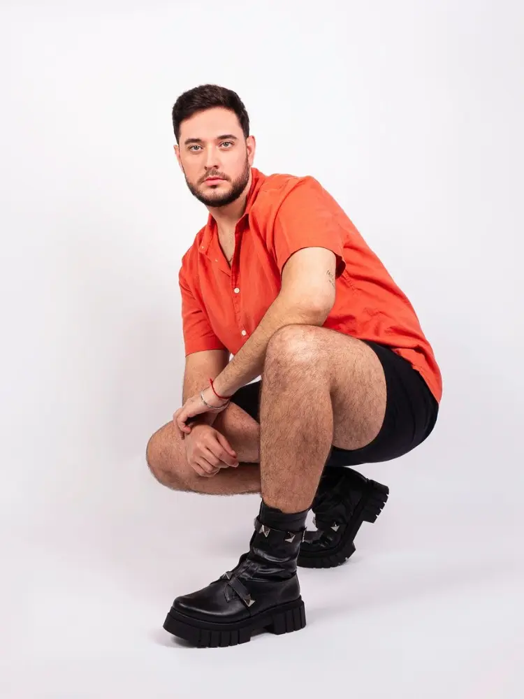 Luis Otavio Pires com camisa laranja, bermuda preta e bota cano baixo preta com fivelas