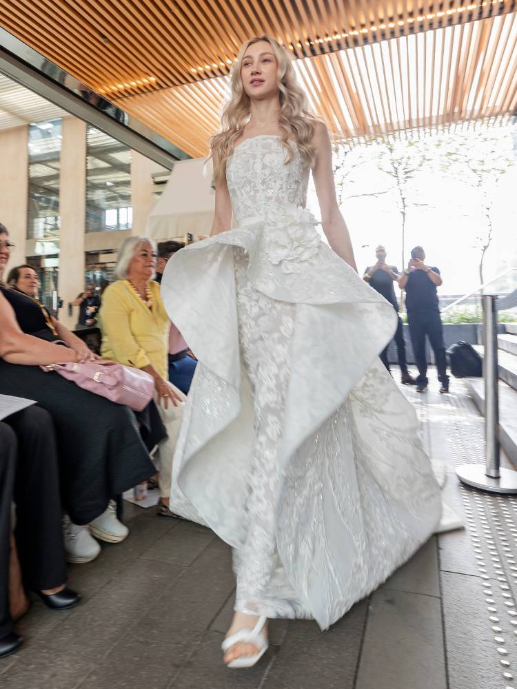 Mulher de pele clara desfilando com vestido de noiva sem alças e com pregas