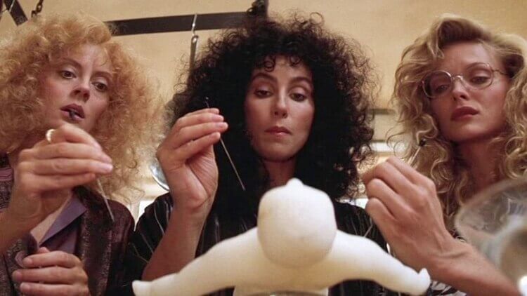 Cena do filme As Bruxas de Eastwick com as protagonistas alfinetando um boneco de vodu Susan Sarandon, Cher e Michelle Pfeiffer em cena do filme de bruxaria "As Bruxas de Eastwick"