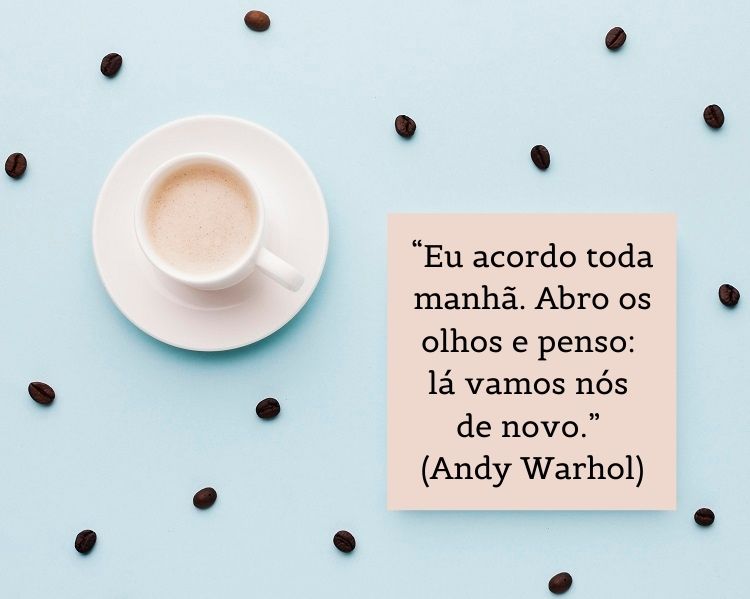 Foto de xícara branca com pires sobre mesa azul com grãos de café e papel com frase “Eu acordo toda manhã. Abro os olhos e penso: lá vamos nós de novo.” (Andy Warhol)