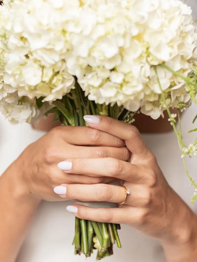Zoom em noiva com unhas brancas segurando buquê de flores brancas