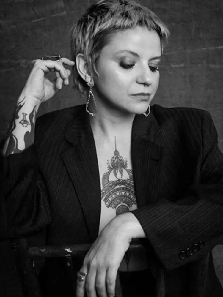 Mulher não-modelo com mais de 40 anos em ensaio fotográfico, usando blazer e joias, sentada em cadeira