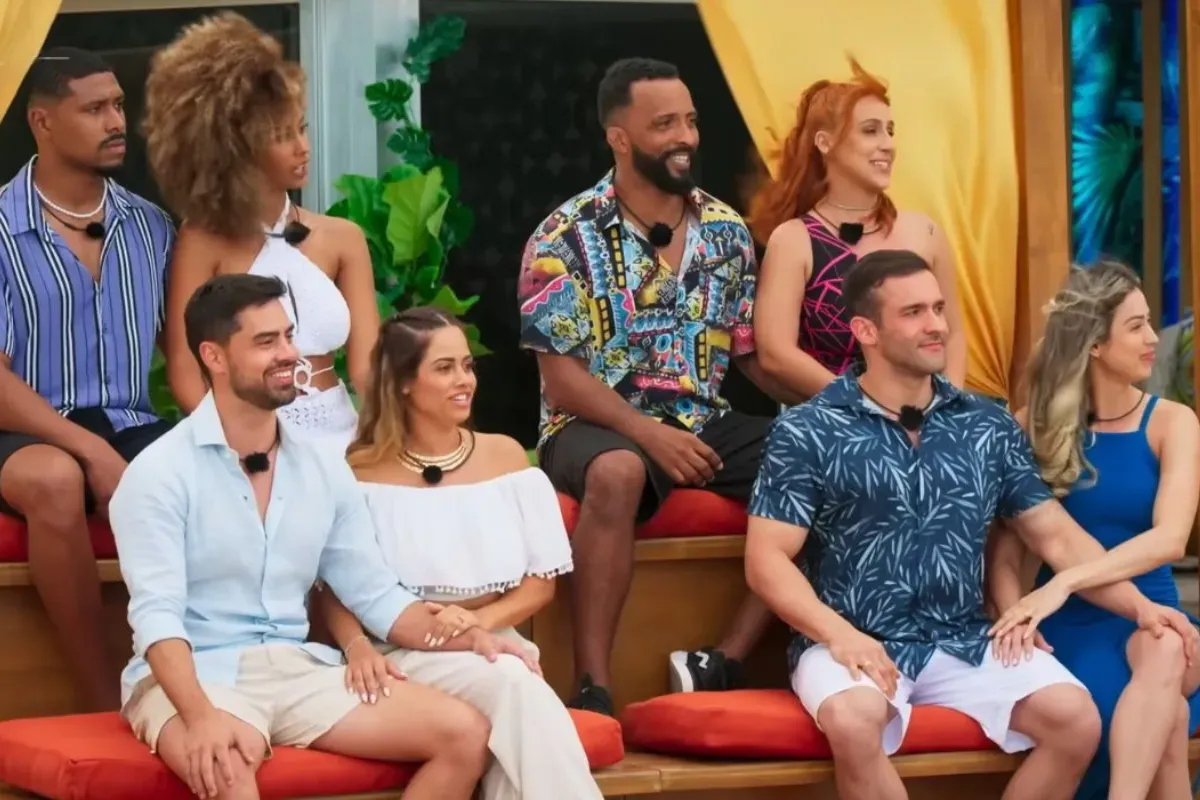 Grupo de participantes sentados durante gravação de reality show de relacionamentos em cenário tropical