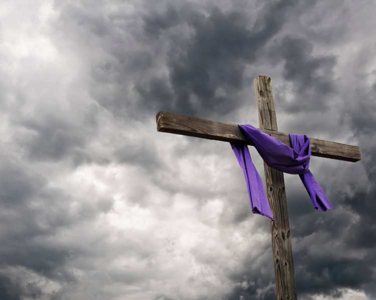 Cruz com pano roxo sob o céu nublado.