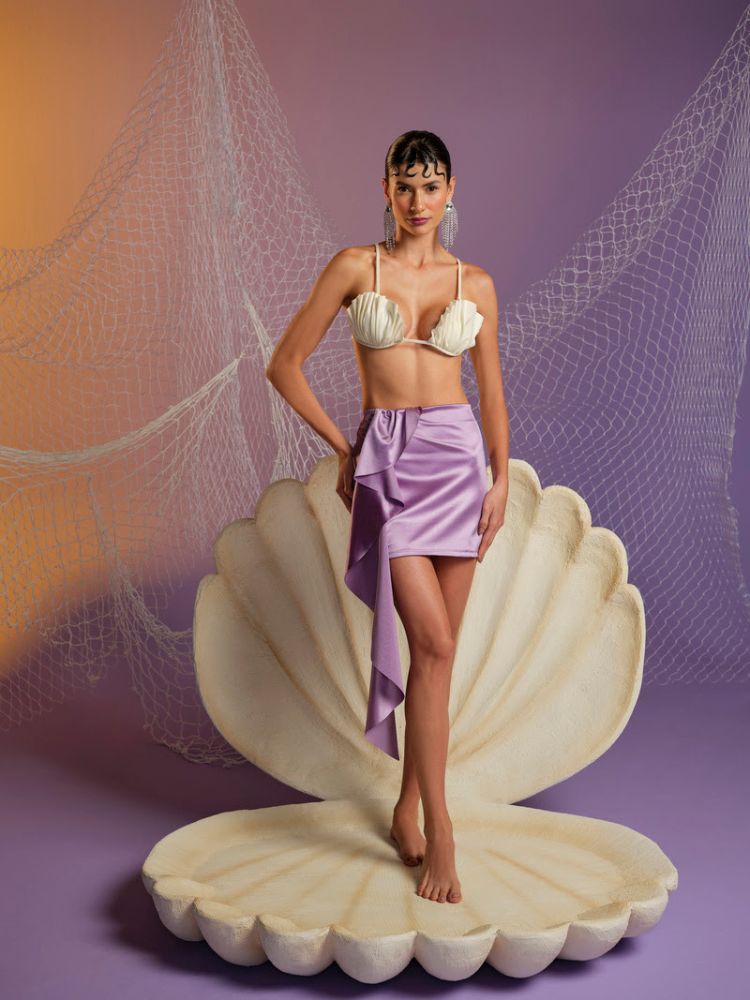 mulher usando top de conchas e saia roxa, fantasia de sereia da coleção de Carnaval 2024 da C&A