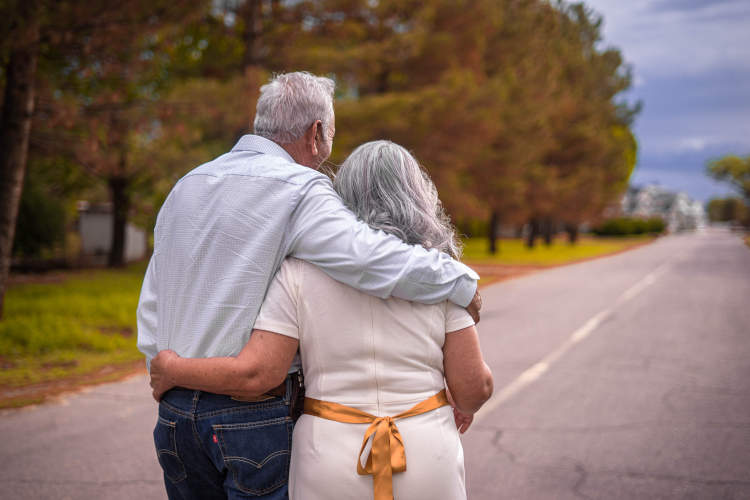foto de casal de idosos na rua, em frente um gramado.