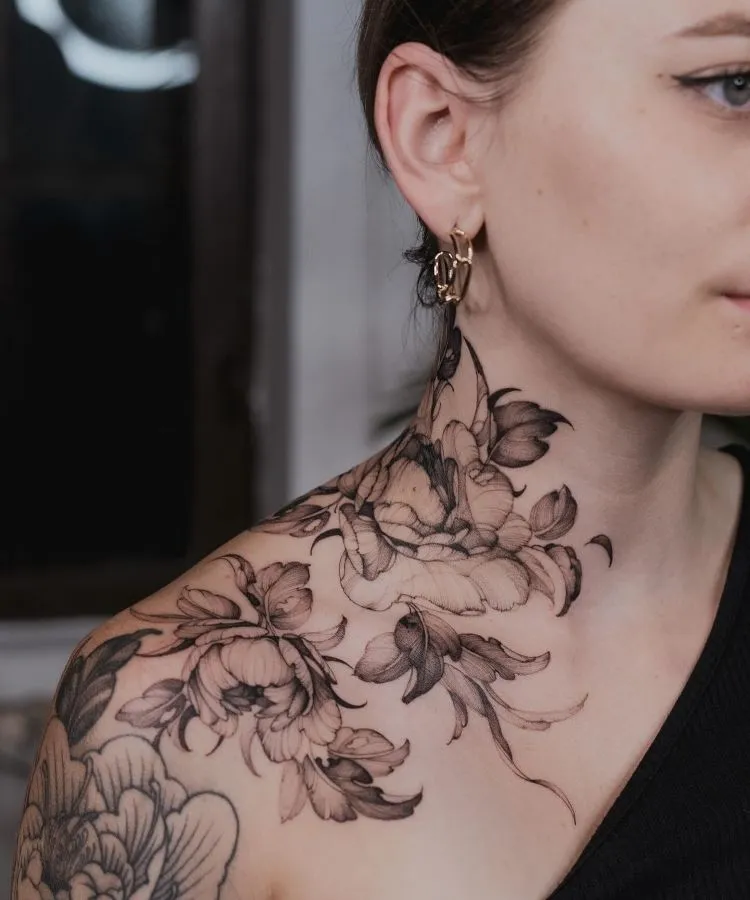A imagem mostra uma pessoa de perfil com cabelo castanho preso. Ela tem uma tatuagem no pescoço de flores detalhadas em preto e cinza, que se estendem até o ombro. A tatuagem é delicada e realista, cobrindo a lateral do pescoço e parte do ombro.


