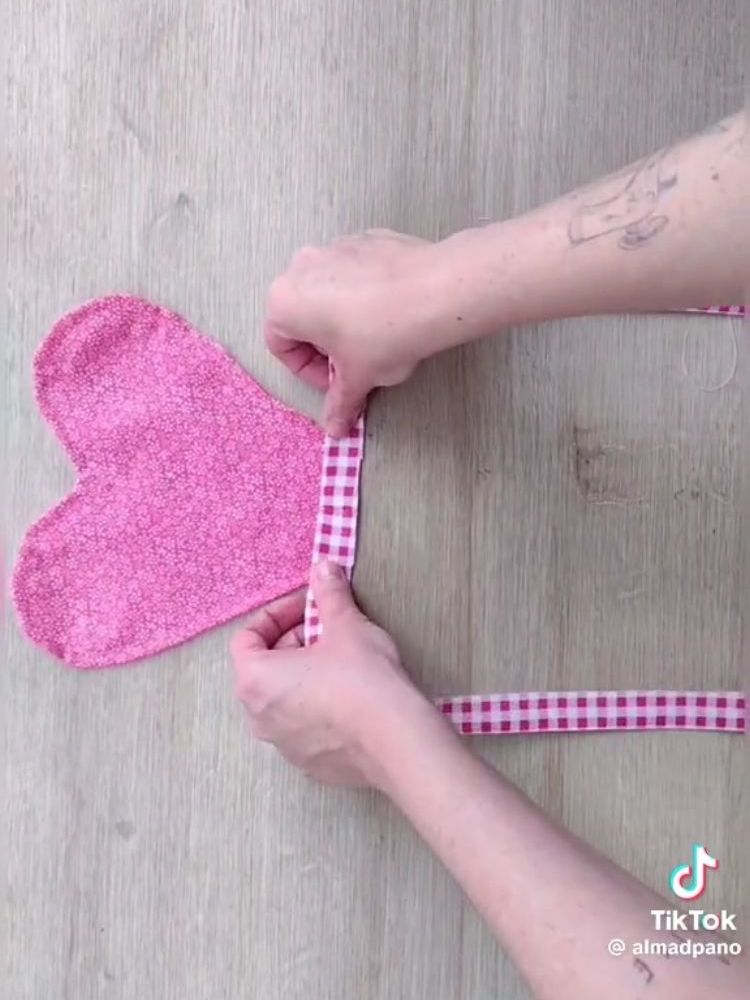 Pessoa de pele clara segurando tecido rosa em formato de coração e faixa xadrez branca e rosa
